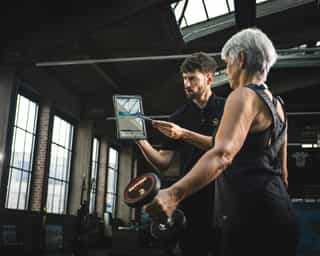 Trainer von Physiosport mit Tablet eläutert einer Frau das Training.