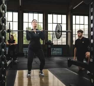 Patientin beim Training mit Langhantel im Krafttrainingsbereich von PhysioSport Köln unter Anleitung eines Trainers.
