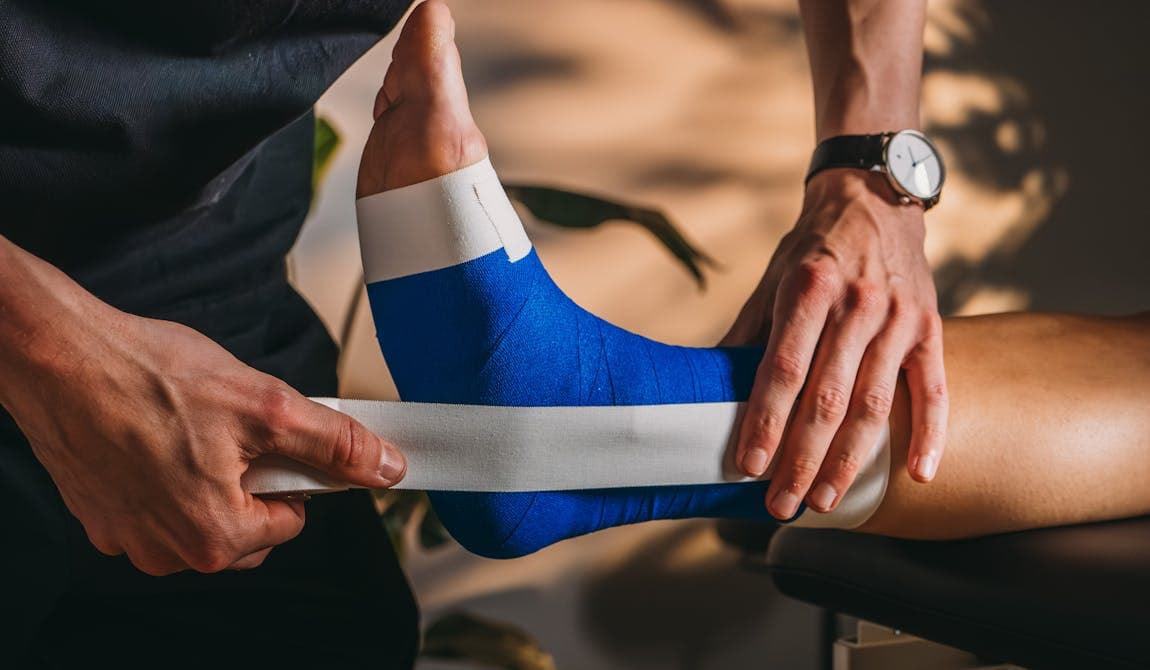 Rechter Fuß einer Patientin wird von Physiotherapeut von PhysioSport Köln getaped.