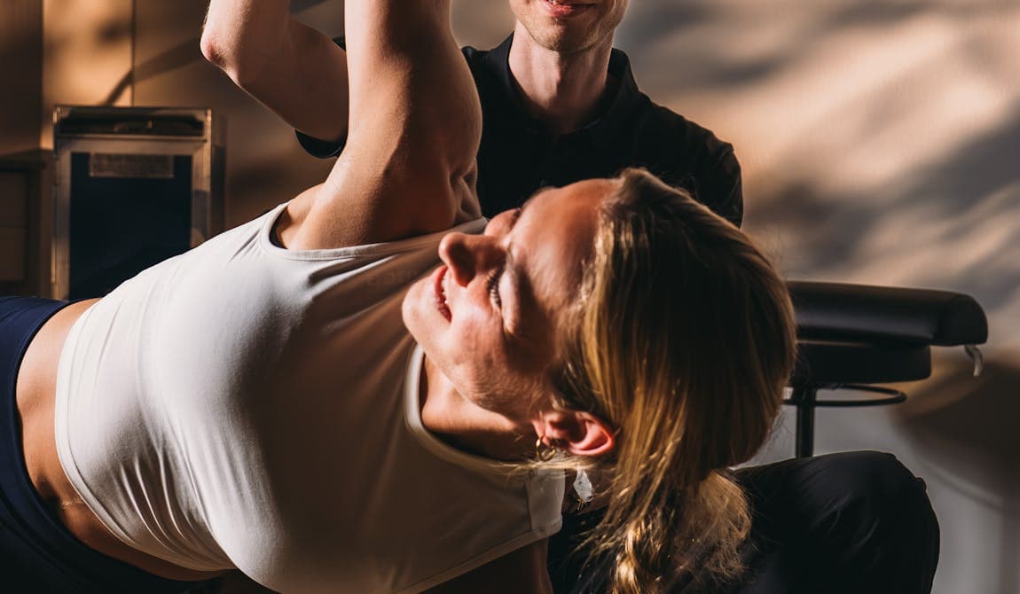 Physiotherapeut von PhysioSport Köln unterstützt Patientin beim Training der Schultermuskulatur.