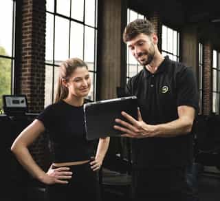 Physiotherapeut von PhysioSport Köln bei Erläuterung von Trainingskonzept am Tablet mit einer Patientin.