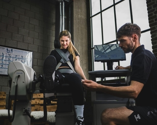 Trainer von PhysioSport Köln erläutert Sportlerin Kraftübungen für die Beinmuskulatur.