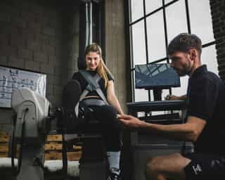 Trainer erläutert Sportlerin bei PhysioSport Köln einige Kraftübungen für die Beinmuskulatur.