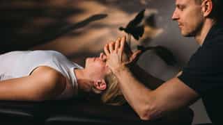 Physiotherapeut von PhysioSport Köln mobilisiert Kopfmuskulatur einer Patientin.