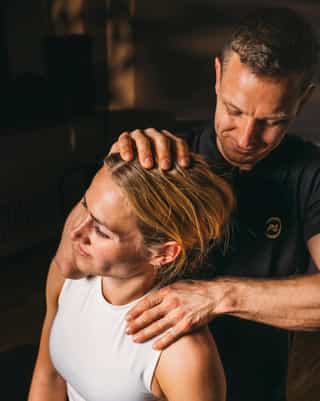 Physiotherapeut von PhysioSport Köln mobilisiert Nackenmuskulatur einer Patientin.