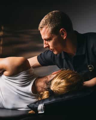 Trainer mobilisiert Rumpfmuskulatur einer Patientin.