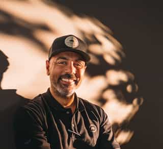 Das Bild zeigt einen Mitarbeiter von Physiosport Kölan, der lächelnd auf einem Fahrrad sitzt.