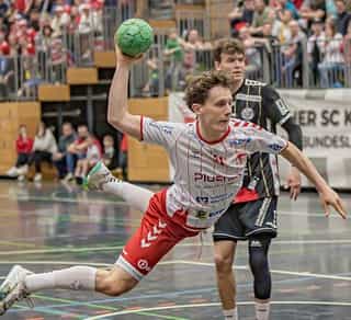 Das Bild zeigt eine Szene aus einem Handballspiel der Herrenmannschaft vom Longericher SC Köln, den Partnern von Physiosport Köln. Zu sehen sind Spieler auf dem Spielfeld und Zuschauer im Hintergrund.