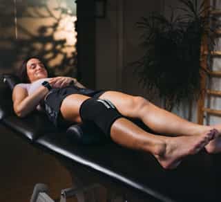 Patientin liegt bei PhysioSport auf Liege mit Kältemanschette am Knie zur Physikalischen Therapie.