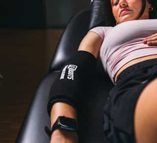 Patientin bei PhysioSport liegt auf Liege, am Ellenbogen ist eine Kältemanschette zur Physikalischen Therapie angebracht.