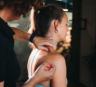 Patientin in Behandlungsraum bei PhysioSport Köln, Therapeutin lokalisiert Nackenpunkte für Behandlung mit Dry Needling.