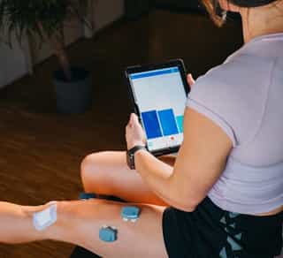 EMG-Behandlung in der Physikalischen Therapie bei PhysioSport Köln, Patientin mit Gerät in der Hand.