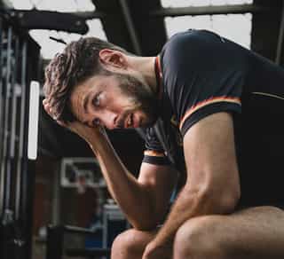 Profisportler sitzt auf einer Bank bei PhysioSport Köln und grübelt über seine Kniebeschwerden nach.