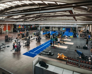 Zu sehen ist die große Trainingsanlage von PhysioSport Köln mit Matten, Geräten und Menschen, die daran trainieren.
