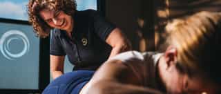 Das Bild zeigt eine Physiotherapeutin, die eine Patientin behandelt. Die Patientin liegt auf einer Behandlungsliege.