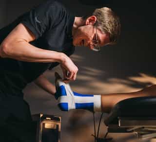 Physiotherapeut beim Tapen eines Sprunggelenks eines Patienten bei Physiosport Köln.