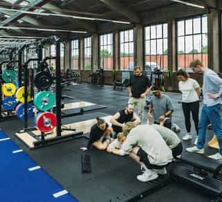 Einblick in die Trainingshalle von Physiosport Köln. Zu sehen sind Trainer und Patienten bei der Erläuterung von Übungen an Trainingsgeräten.
