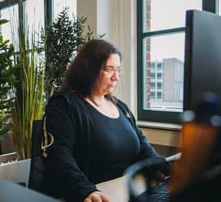 Zu sehen ist der Einblick in einen offenen Arbeitsplatz bei PhysioSport Köln. Dort sitzt eine Mitarbeiterin konzentriert am Computer.