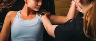 Zu sehen ist eine Physiotherapeutin von Physiosport Köln bei der Behandlung einer Patientin mit Impingement Schulter. Die Patientin liegt dabei flach auf dem Rücken.