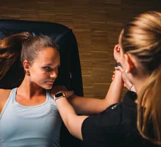 Zu sehen ist eine Physiotherapeutin von PhysioSport Köln bei der Behandlung einer Patientin mit Impingement Schulter. Die Patientin liegt dabei flach auf dem Rücken.