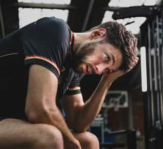 Profisportler sitzt auf einer Bank im Trainingsraum und denkt über seine Schmerzen nach.