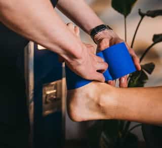 Physiotherapeut von Physiosport Köln taped ein Sprunggelenk eines Sportlers.