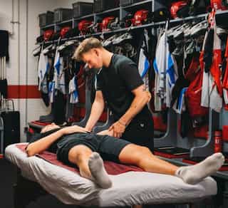 Profisportler auf einer Liege wird behandelt. Physiotherapeut von PhysioSport spricht mit Sportler über Beschwerden an der Kniescheibe.