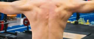 Zu sehen ist ein muskolöser Sportler bei der Beschwerdeanalyse von einem Physiotherapeuten auf der Trainingsanlage von PhysioSport Köln.