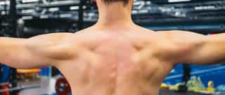 Zu sehen ist ein muskolöser Sportler bei der Beschwerdeanalyse von einem Physiotherapeuten auf der Trainingsanlage von PhysioSport Köln.