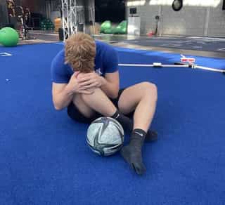 Man sieht einen Sportler bei PhysioSport Köln, schräg von vorne gesehen, der sich vor Schmerzen an sein Knie fasst.