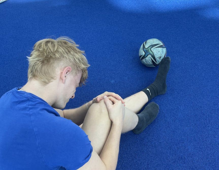 Man sieht einen Sportler bei PhysioSport Köln, schräg von hinten gesehen, der sich vor Schmerzen an sein Knie fasst.