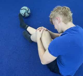 Zu sehen ist ein Sportler bei PhysioSport Köln, der sich vor Schmerzen an sein Knie fasst.