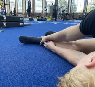 Sportler liegt mit Schmerzen am Boden bei PhysioSport Köln und fasst sich mit den Händen an sein Sprunggelenk.