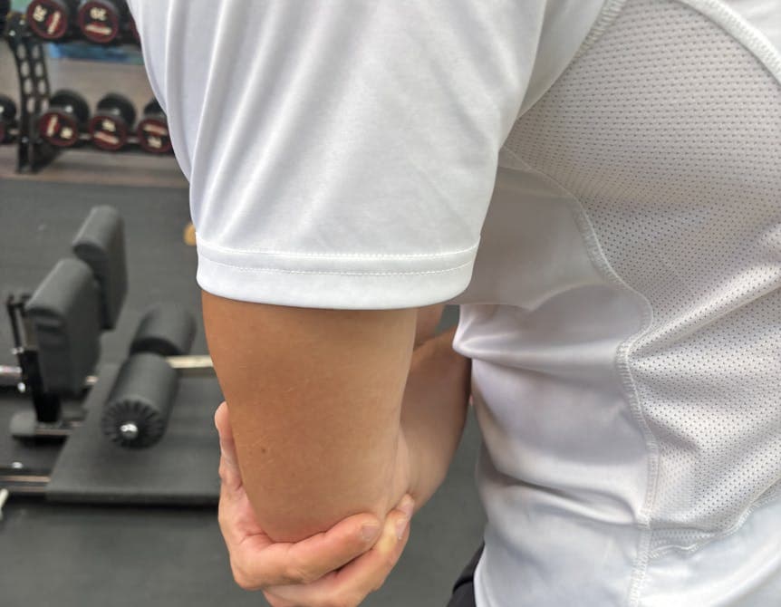 Man sieht einen Sportler mit Schmerzen am Ellenbogen, Tennisellenbogen Behandlung bei PhysioSport Köln.