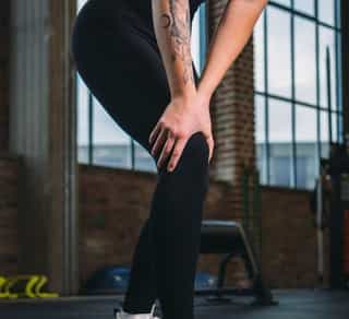 Sportlerin fasst sich an ihr rechtes Knie aufgrund von Knieschmerzen nach Sportunfall.