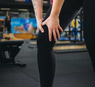 Sportlerin fasst sich ans Knie aufgrund von Knieschmerzen.