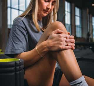 Sportlerin fasst sich ihr rechtes Knie aufgrund von Knieschmerzen.