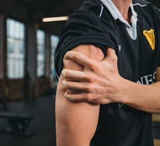 Sportler zeigt die genauen Schmerzstellen an der Schulter bei PhysioSport Köln.